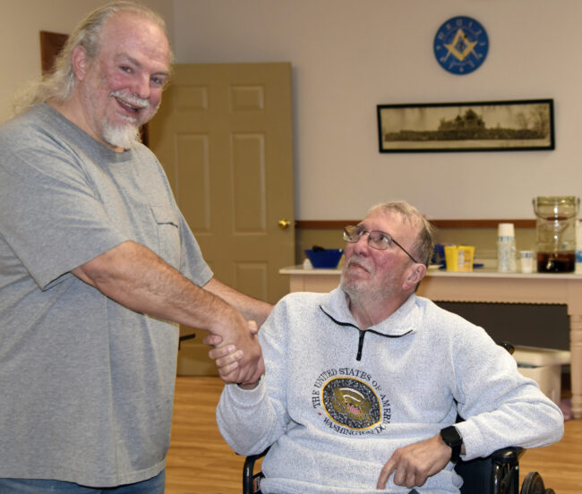 Winner Frank Austin, seated center-right, shakes hands with board member Bret Greenwood, standing, left.