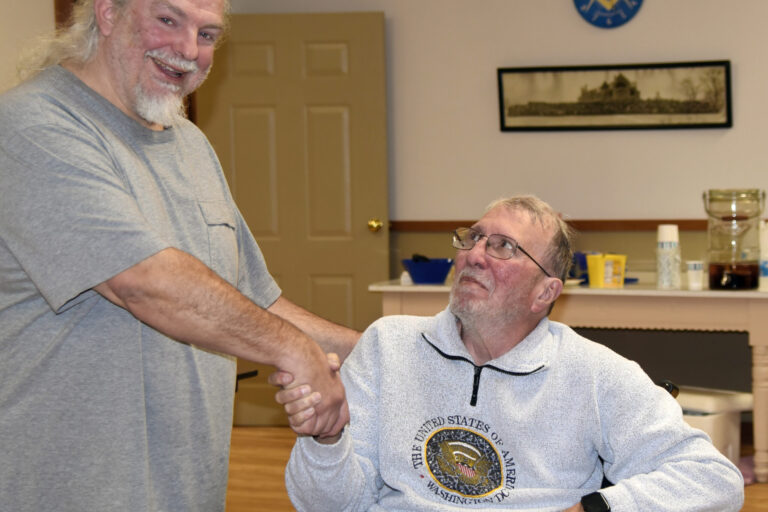 Winner Frank Austin, seated center-right, shakes hands with board member Bret Greenwood, standing, left.